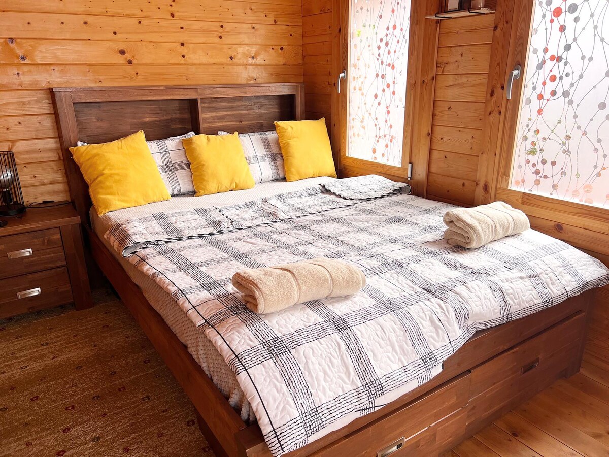 The bedroom at Auckland Airport Cabin, with a queen bed, warm wood walls and yellow cushions.
